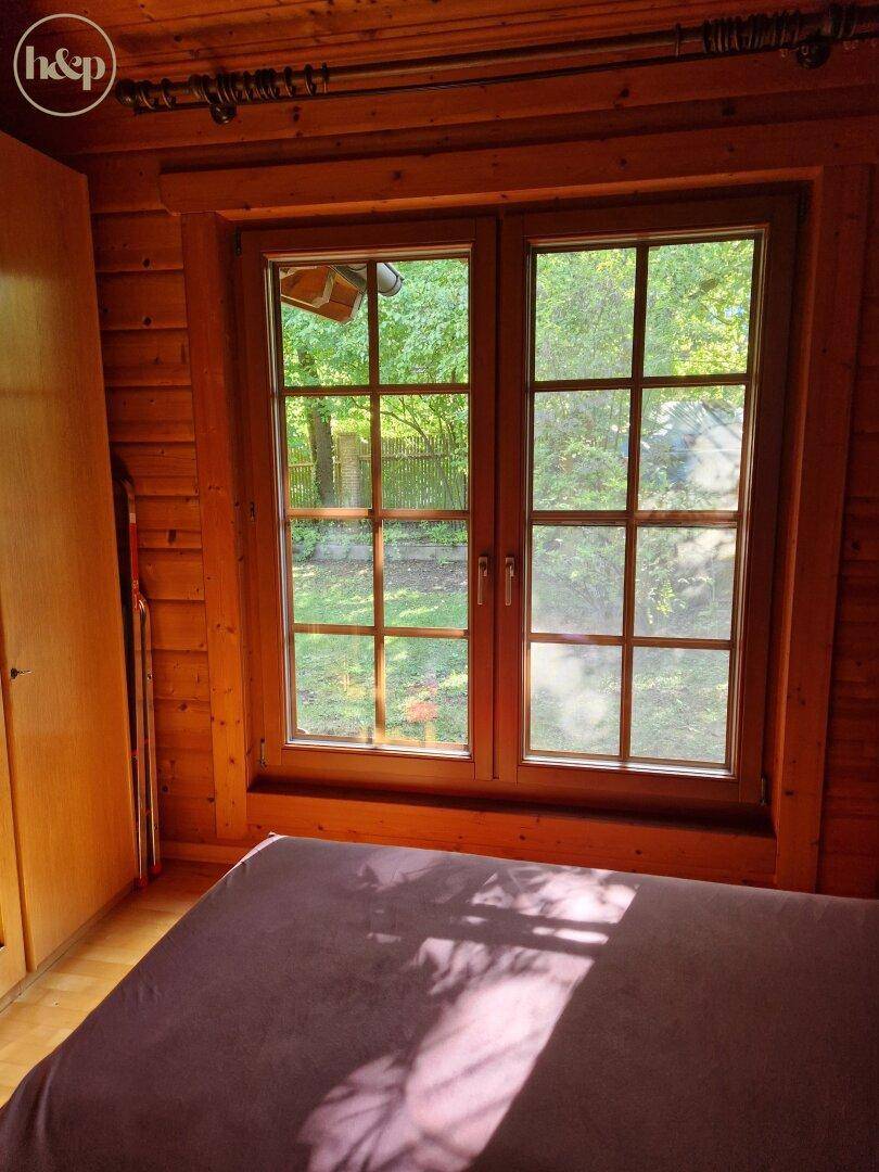 Gemütliches Schlafzimmer mit Holzwänden, großen Fenstern und Blick ins Grüne.