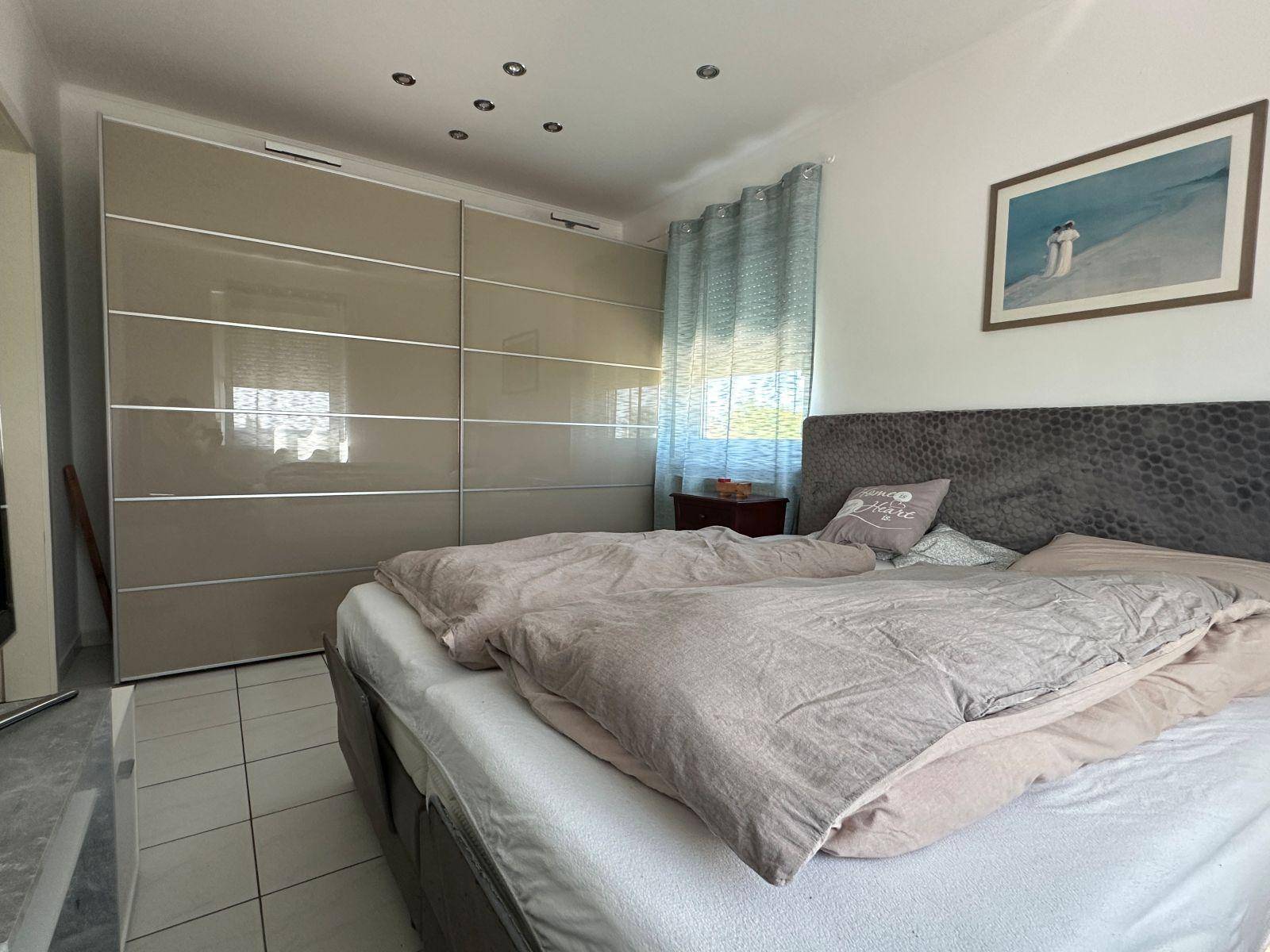 Schlafzimmer mit großem Bett und glänzendem Einbauschrank, ideal für Stauraum.