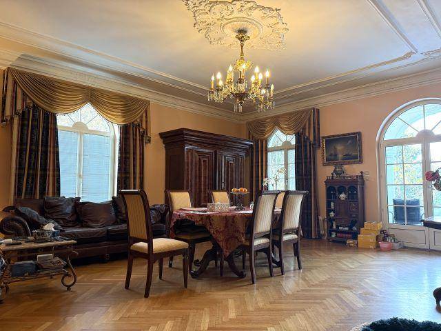 Elegantes Wohn-Esszimmer mit Fischgrätparkett, Stuckdecke und großen Rundbogenfenstern.