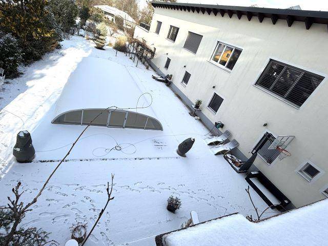 Seitenansicht des Hauses mit überdachtem Poolbereich und verschneitem Garten im Winter.