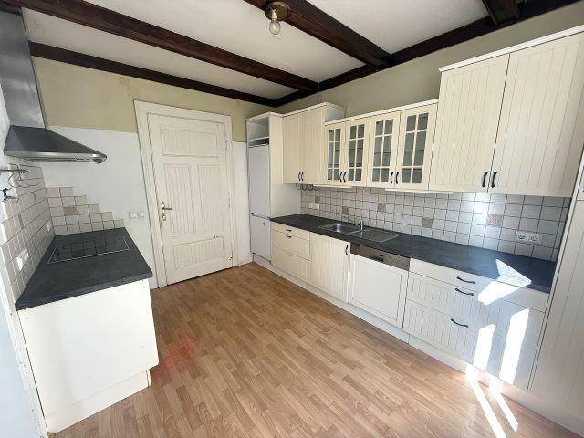 Funktionale Küche mit weißen Schränken, Holzbalken und Fliesenrückwand, bereit zur Modernisierung.