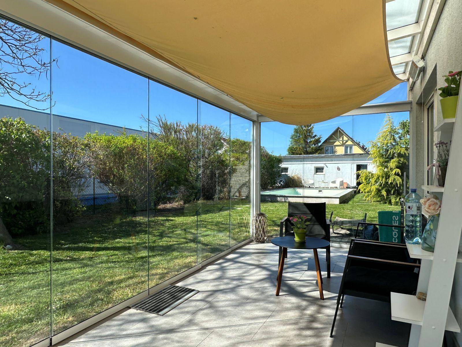 Verglaster Wintergarten mit Sitzgelegenheiten und weitem Blick auf den Garten und Pool.