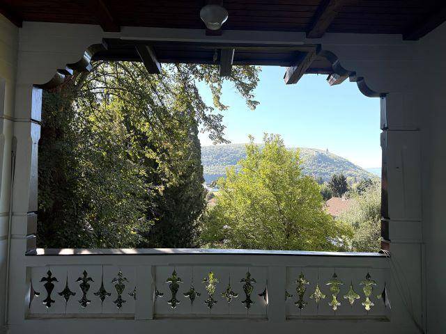 Blick von der Loggia mit kunstvollem Geländer auf die grüne Hügellandschaft und den blauen Himmel.