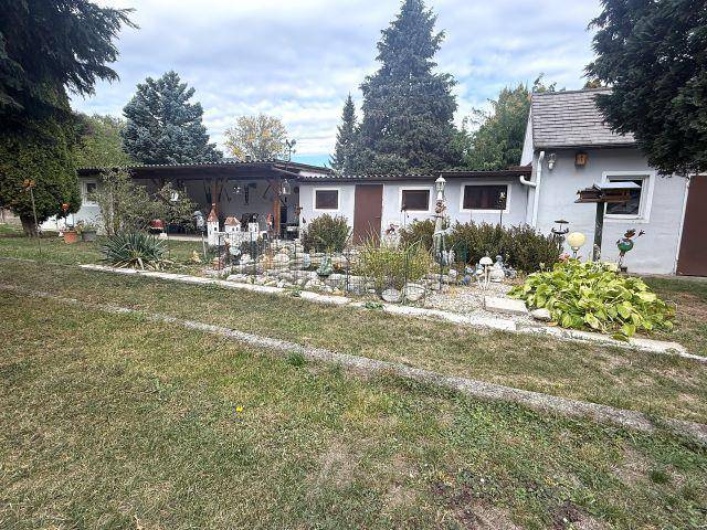 Weitläufiger Garten mit Rasenfläche, Zierbeeten und einem überdachten Sitzbereich im Hintergrund.