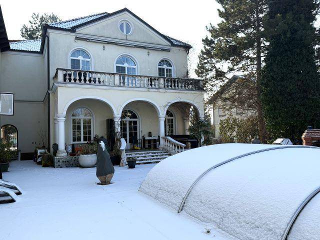 Rückseite der Villa mit großem Balkon, überdachtem Poolbereich und verschneitem Garten.