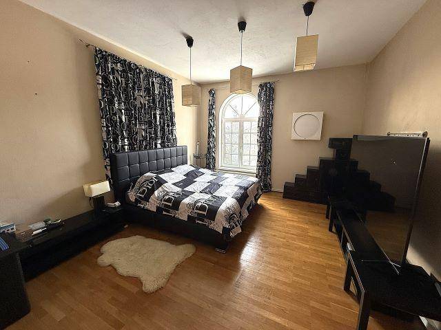 Schlafzimmer mit Parkettboden, gemusterten Vorhängen und großem Fenster.