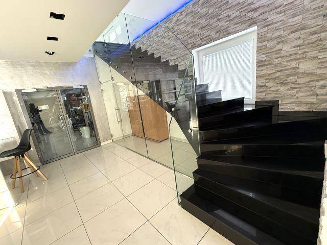 Moderner Eingangsbereich mit glänzenden Fliesen, Glasgeländer und schwarzer Treppe.