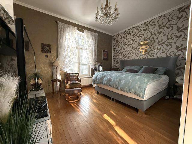 Gemütliches Schlafzimmer mit Parkettboden, gemusterter Tapete und Kronleuchter.