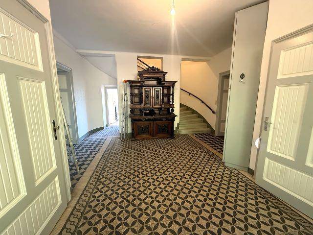 Geräumiger Flur mit historischen Fliesenböden und einer eleganten Holztreppe, die in die oberen Stockwerke führt.