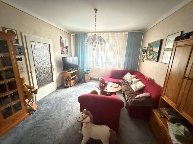 Wohnzimmer mit rotem Sofa, Teppichboden und einem Fenster mit Vorhängen.