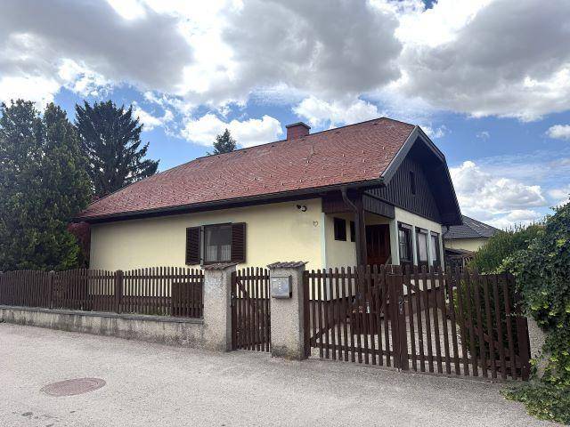 Traditionelles Einfamilienhaus mit rotem Ziegeldach und Holzzaun, von der Straße aus gesehen.