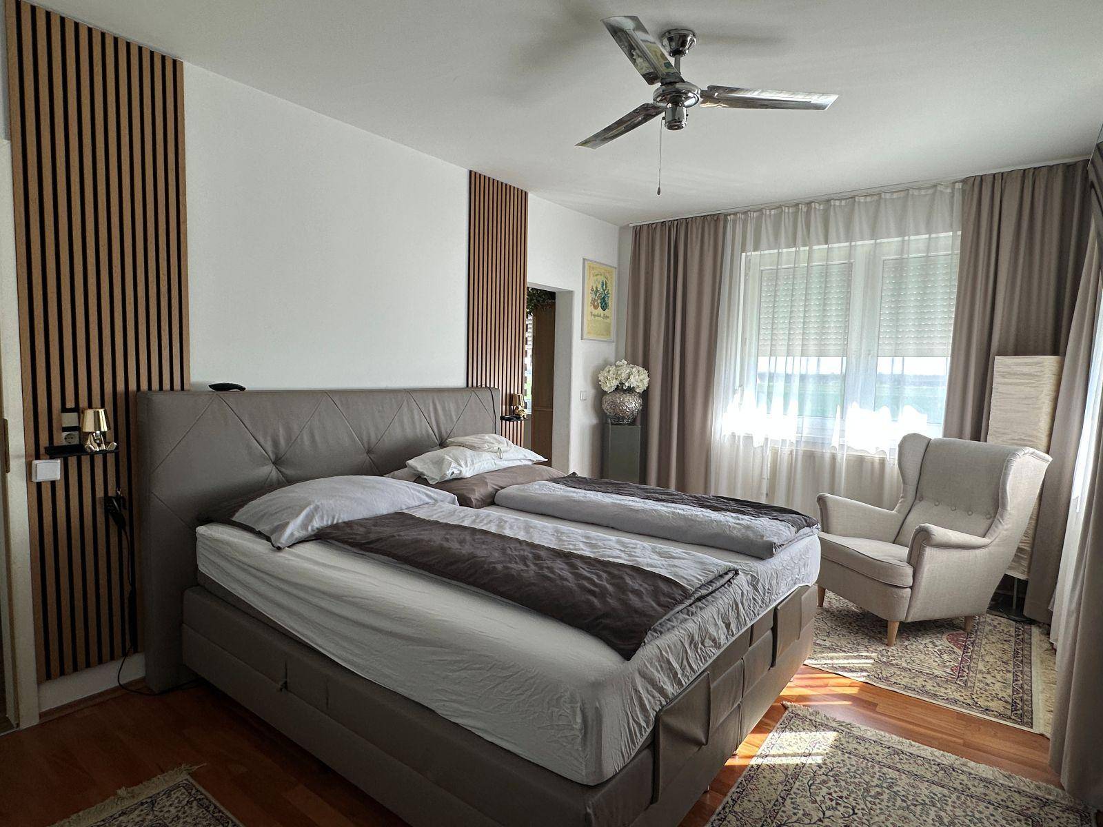 Geräumiges Schlafzimmer mit großem Bett, Holzakzentwand und Deckenventilator.