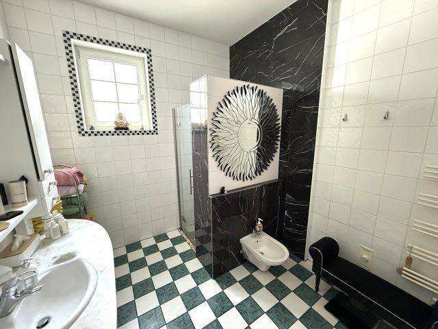 Helles Badezimmer mit Schachbrettmuster-Fliesen, Dusche, Bidet und Fenster.