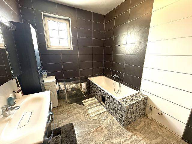 Modernes Badezimmer mit dunklen Fliesen, Badewanne und Fenster.