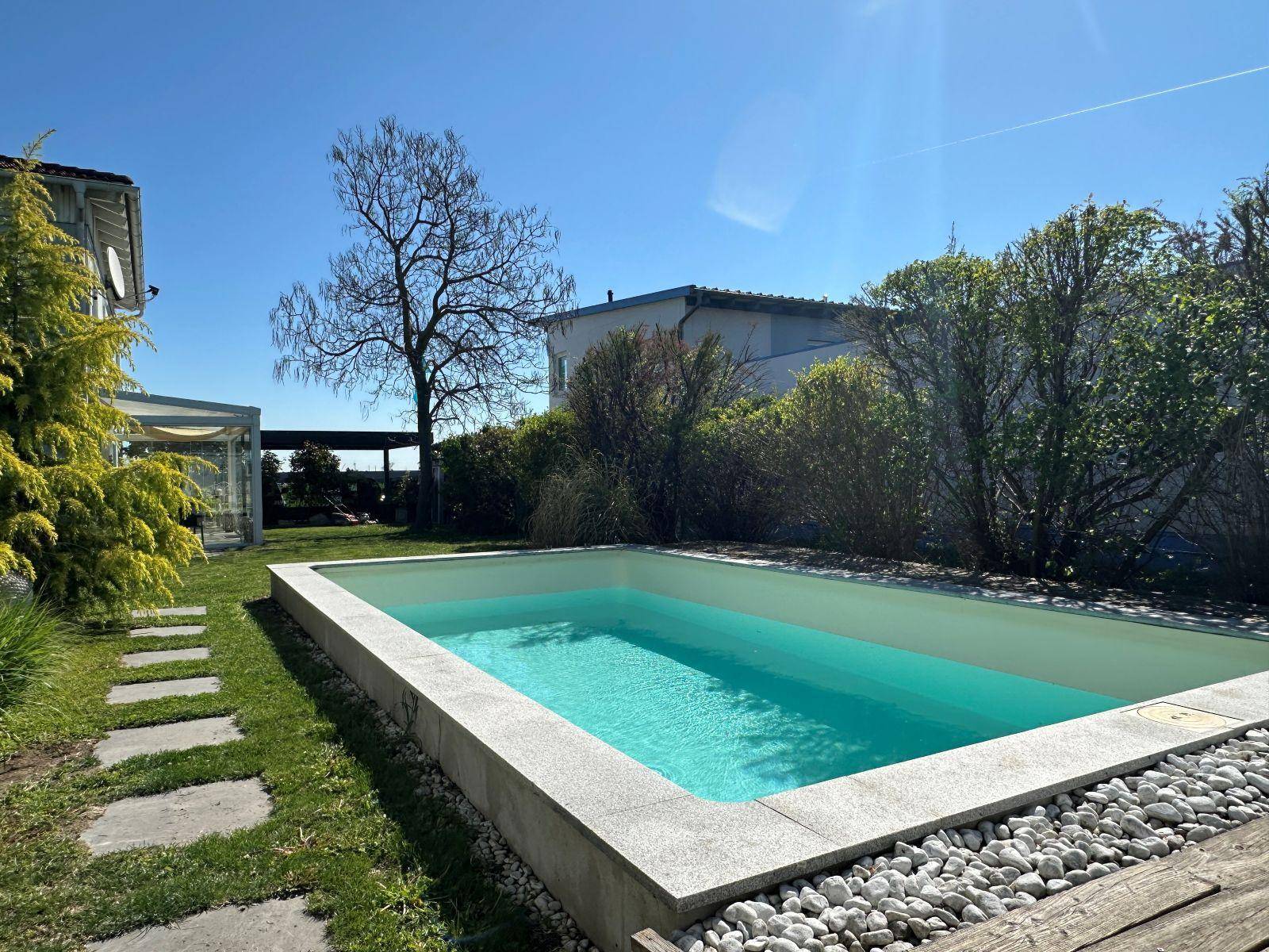 Gepflegter Gartenbereich mit rechteckigem Pool, Rasenfläche und sonniger Atmosphäre.