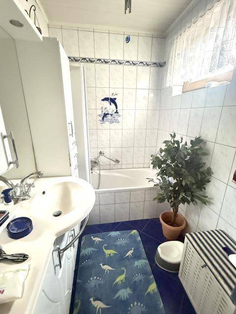 Helles Badezimmer mit Badewanne, Waschbecken und blauen Akzenten in den Fliesen.