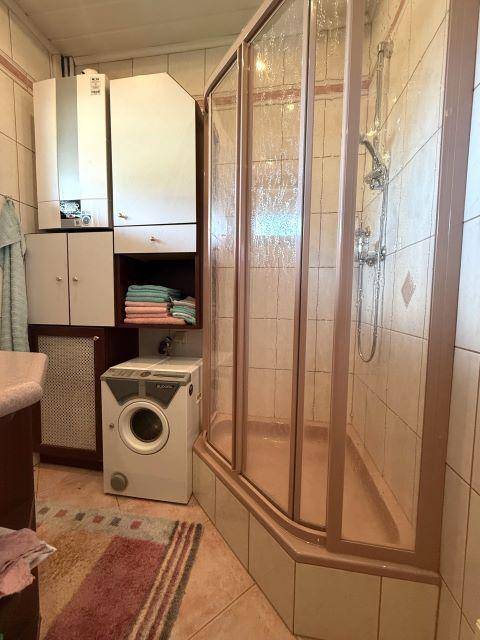 Funktionales Badezimmer mit Duschkabine, Waschmaschine und Heizungsanlage.