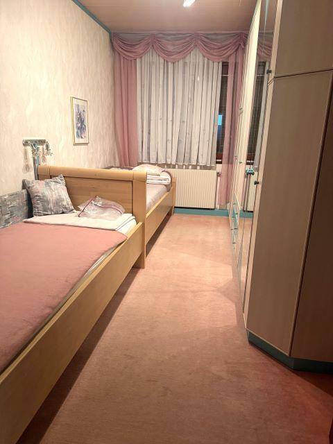 Schlafzimmer mit zwei Einzelbetten, Teppichboden und rosa Vorhängen.