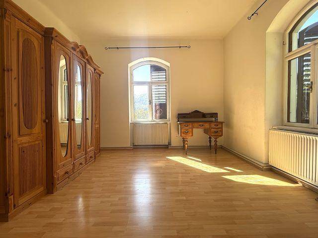 Geräumiges Schlafzimmer mit Holzboden und großem Holzschrank, hell durch die Fenster mit Ausblick.