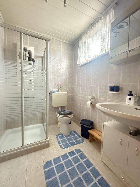 Badezimmer mit Duschkabine, WC, Waschbecken und hellen Fliesen.