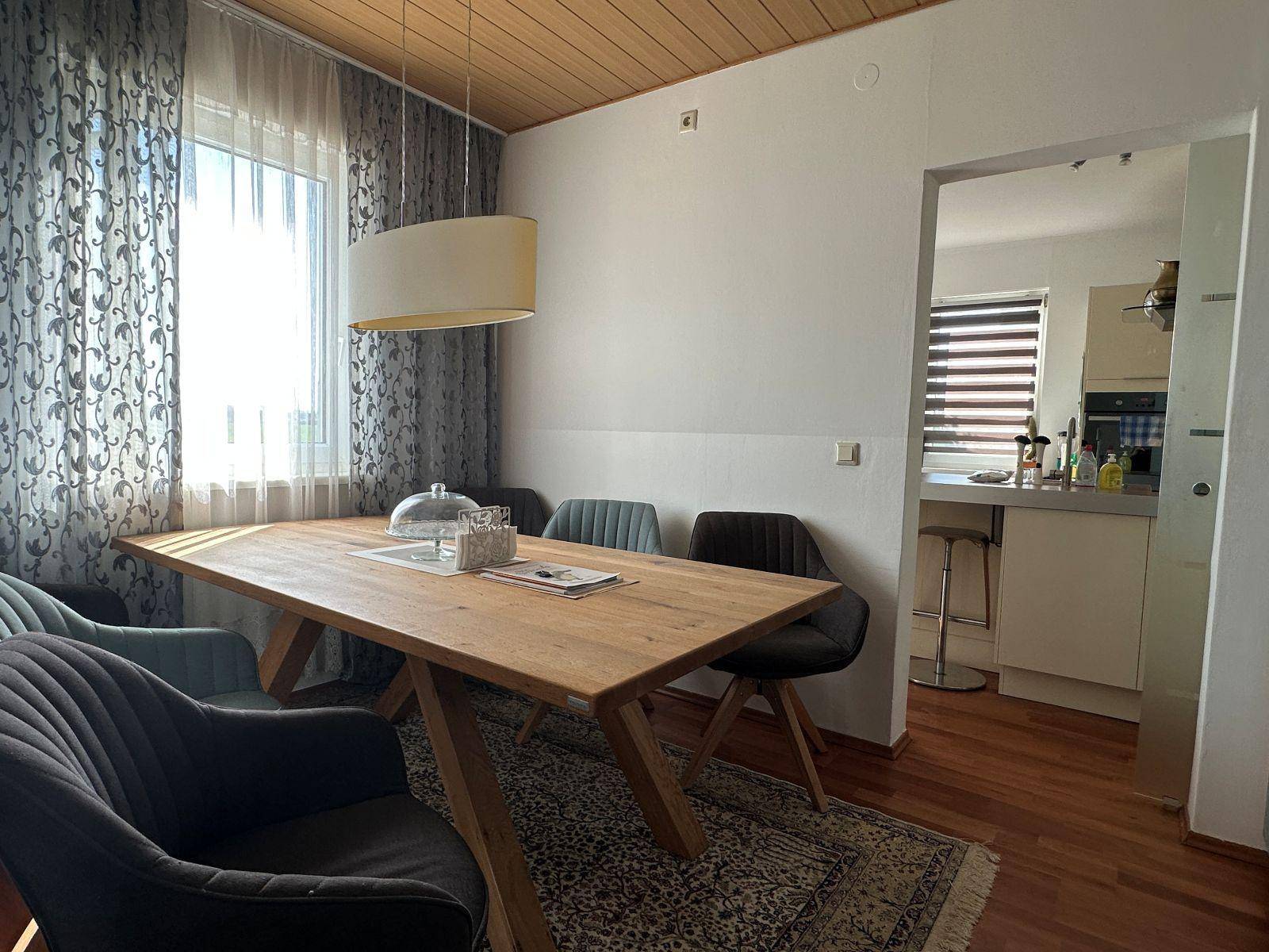 Gemütliches Esszimmer mit großem Holztisch, modernen Stühlen und Blick in die Küche.