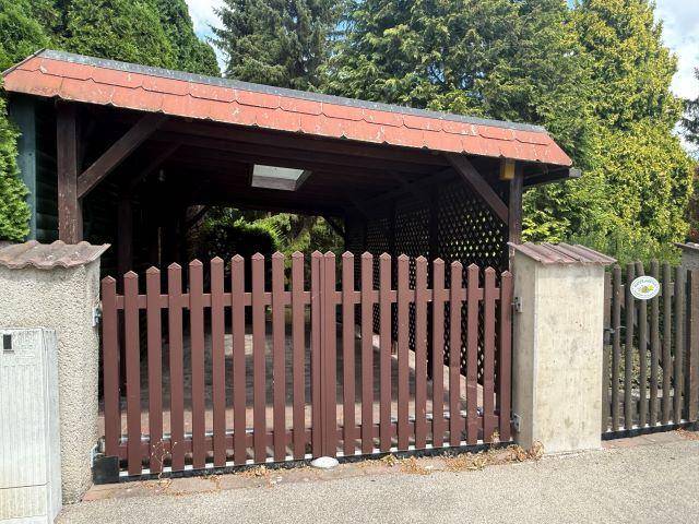 Holz-Carport mit Satteldach und abschließbarem Tor.