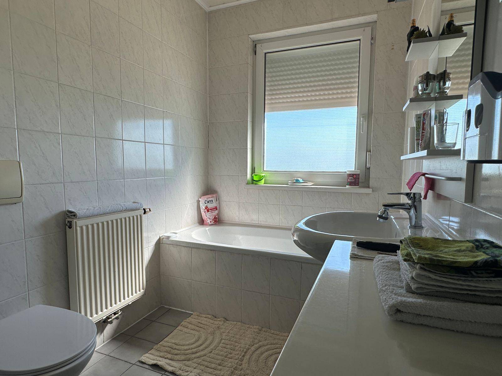 Helles Badezimmer mit Badewanne, WC, Waschbecken und Fenster für Tageslicht.
