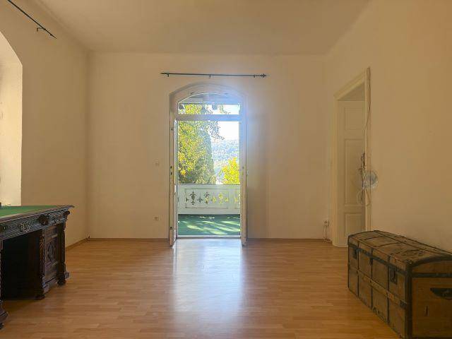 Heller Raum mit Holzboden und Zugang zu einem Balkon, der einen weiten Blick in die Natur bietet.