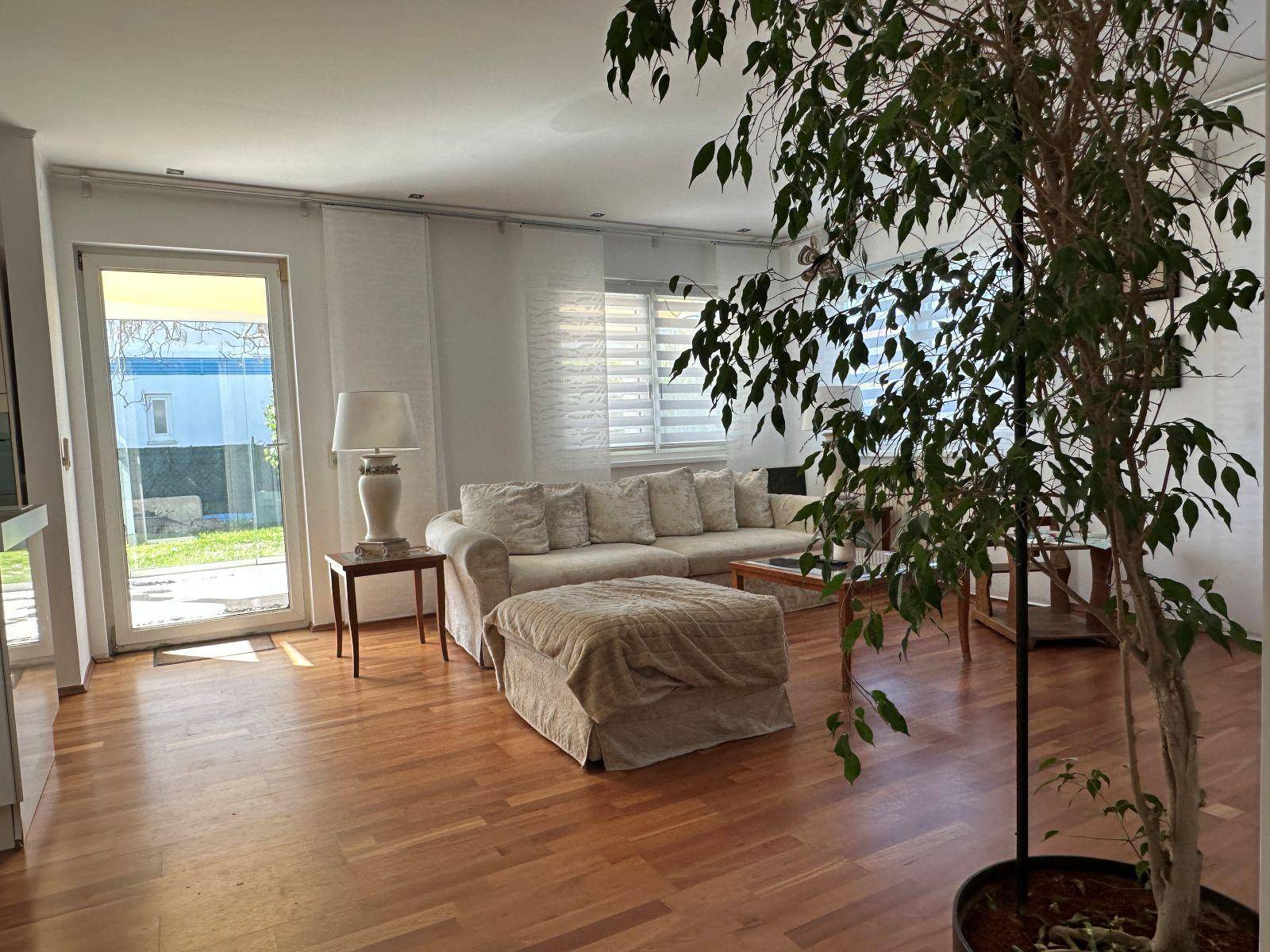Lichtdurchflutetes Wohnzimmer mit Holzboden, bequemer Couch und direktem Zugang zum Garten.