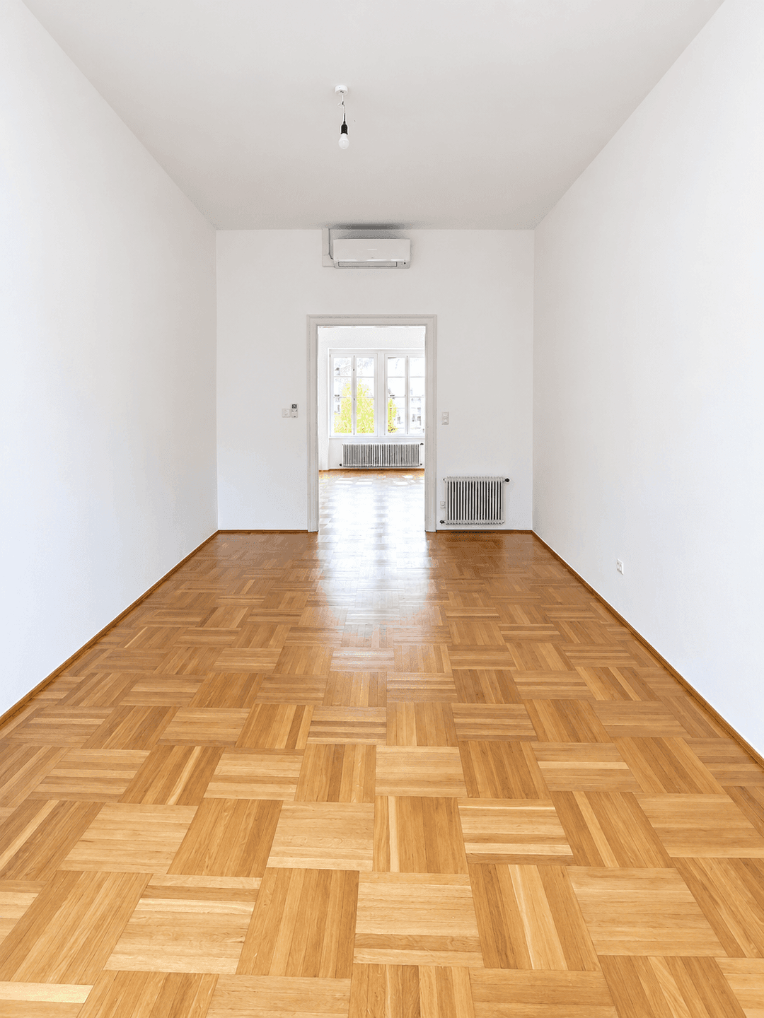 Langer, heller Flur mit Parkettboden und Blick durch eine Tür in einen weiteren Raum.