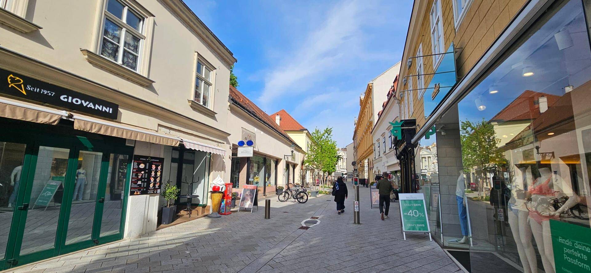 Eine charmante Fußgängerzone mit Geschäften und historischen Gebäuden unter einem klaren blauen Himmel.