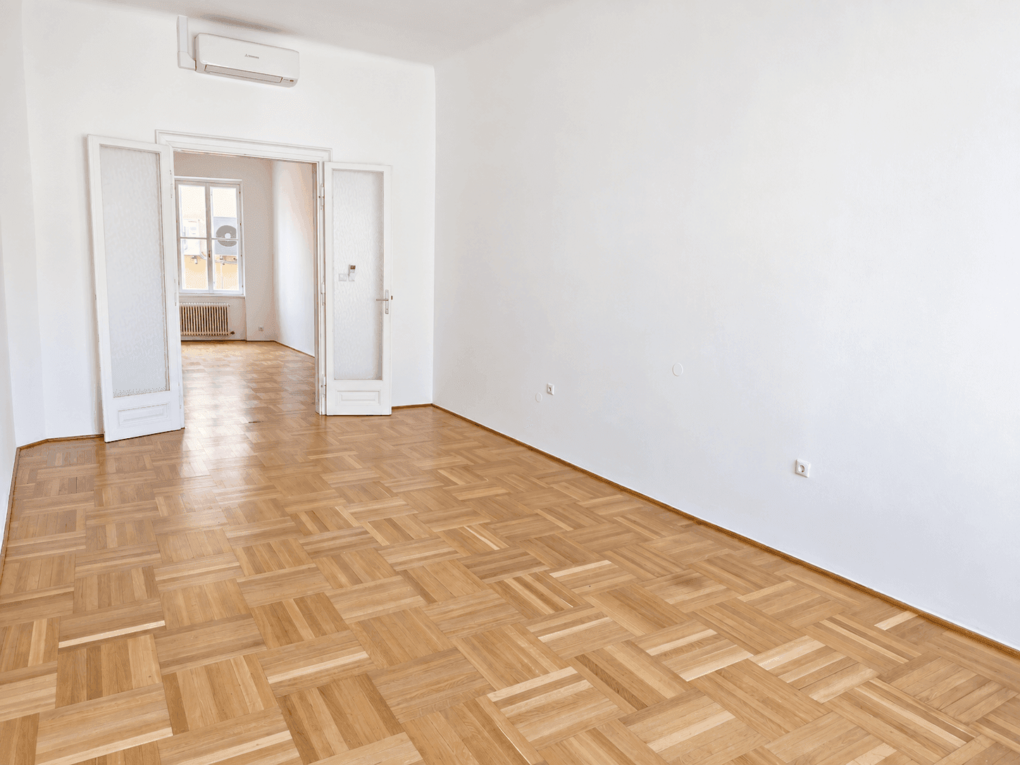 Heller Flur mit Parkettboden und Doppeltüren, die zu einem weiteren Raum führen.