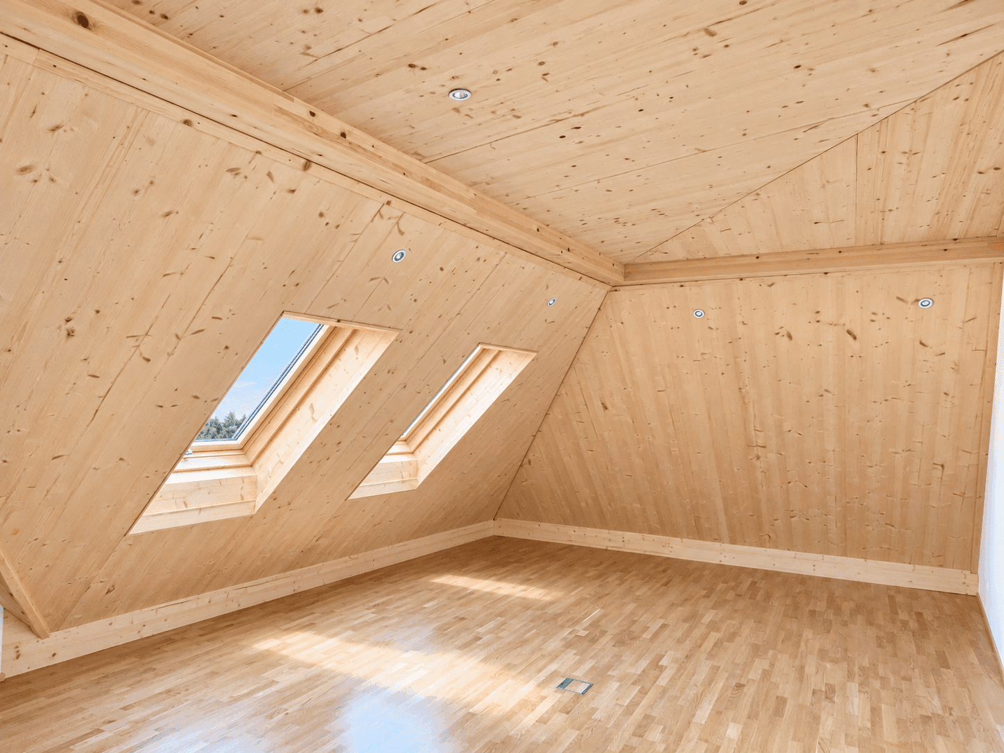 Dachgeschossraum mit Holzverkleidung, schrägen Wänden und zwei Dachfenstern für viel Licht.