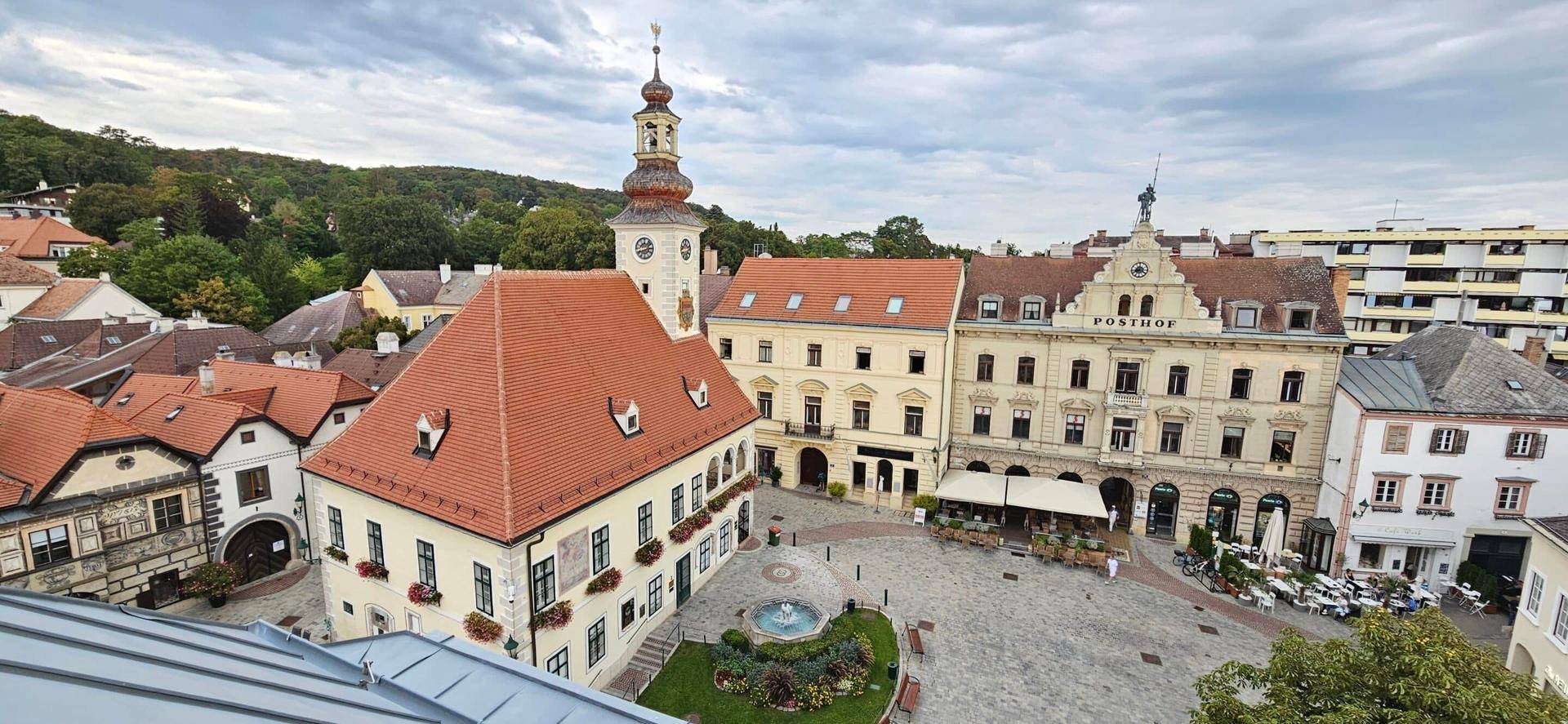 Panoramablick über einen historischen Stadtplatz mit Kirche und traditionellen Gebäuden unter bewölktem Himmel.
