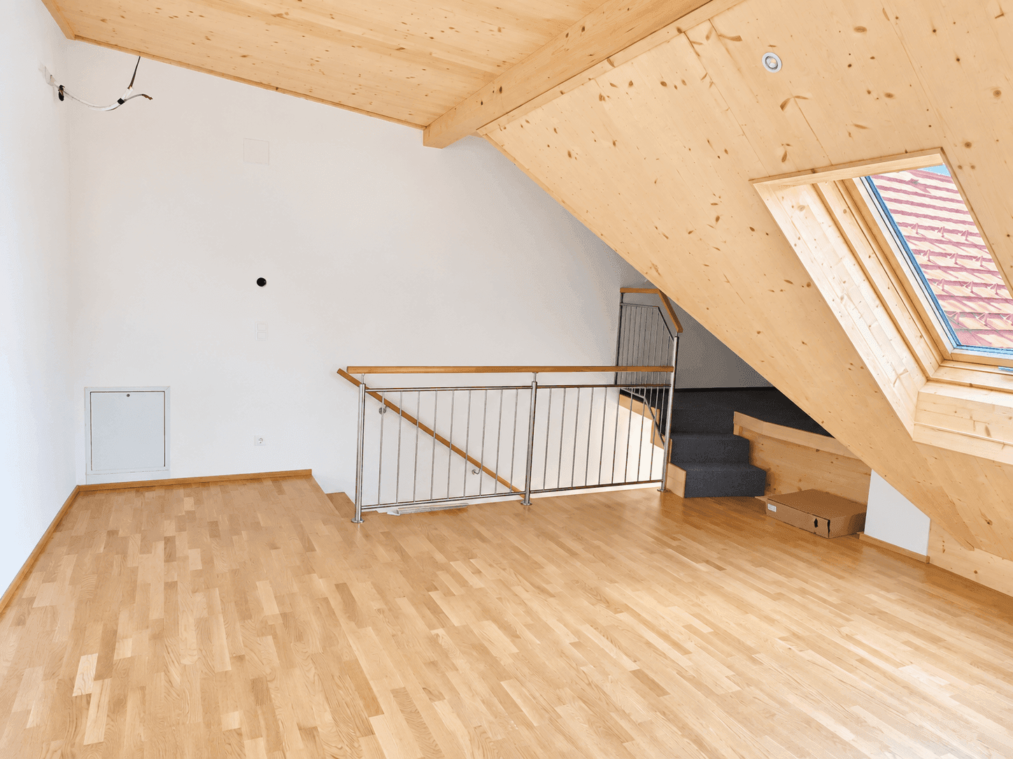 Geräumiges Dachgeschoss mit Holzboden, schrägen Wänden und einem Dachfenster.