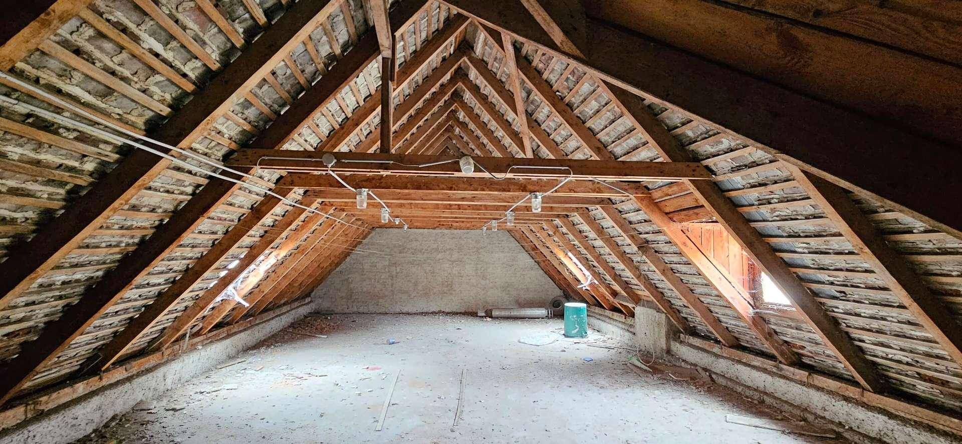 Unausgebauter Dachboden mit sichtbarer Holzkonstruktion des Dachstuhls und einem kleinen Fenster.