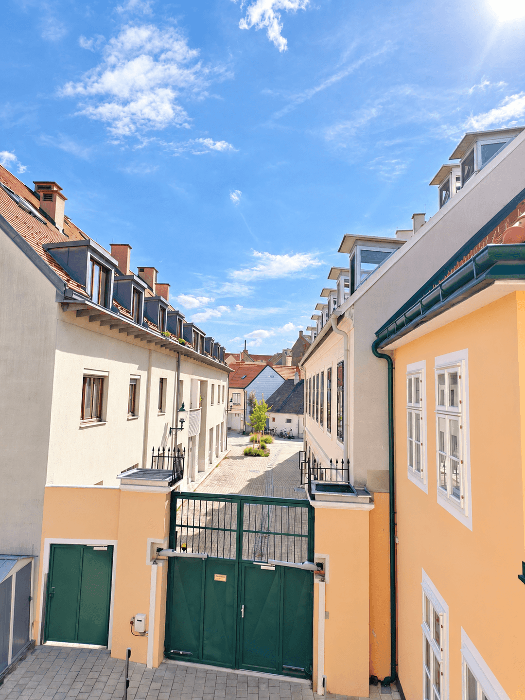 Enger Durchgang zwischen historischen Gebäuden mit einem grünen Tor, das zu einem Innenhof führt.