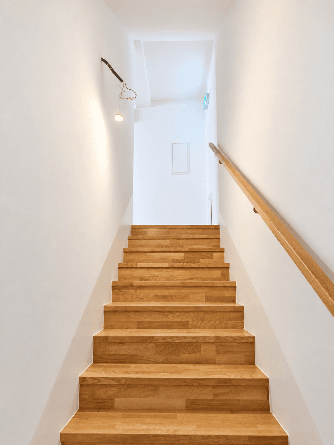 Holztreppe mit hellem Geländer führt nach oben, beleuchtet von einer provisorischen Lampe.
