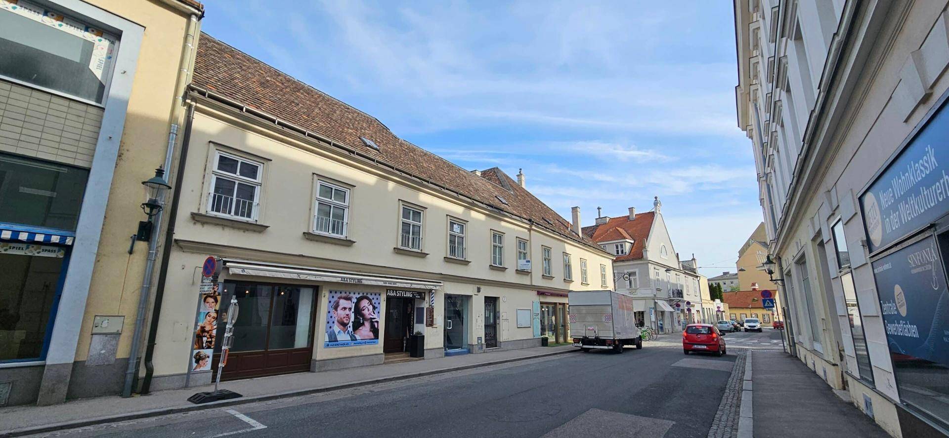 Blick auf eine belebte Straße mit historischen Gebäuden und Geschäften unter einem blauen Himmel.