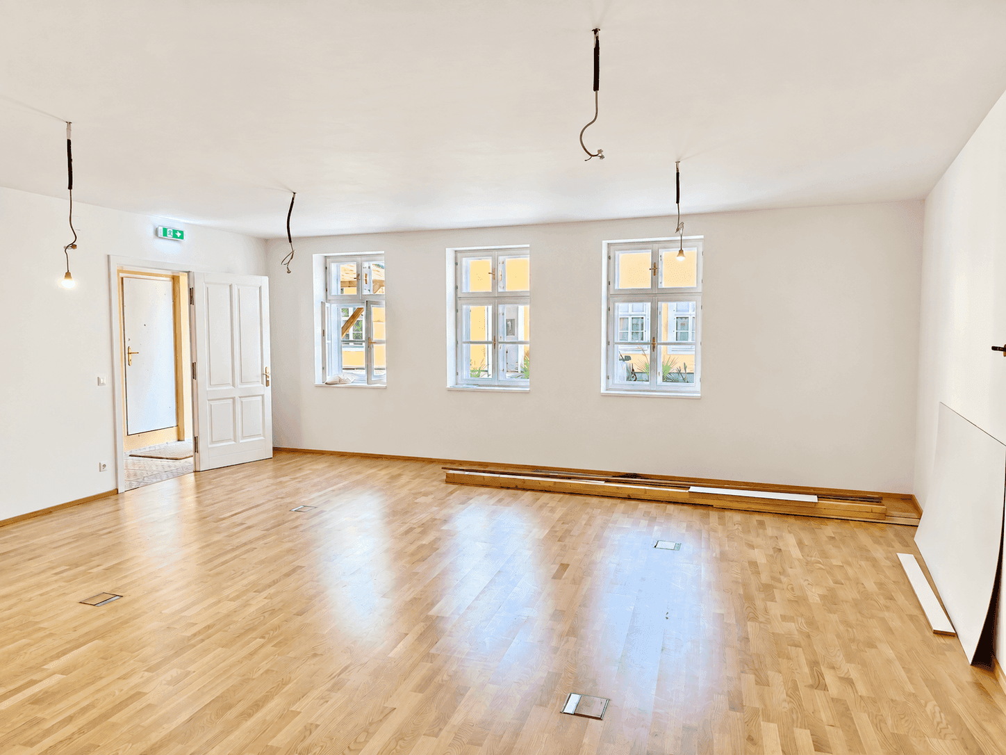 Geräumiger, heller Raum mit Parkettboden, mehreren Fenstern und einer offenen Tür.