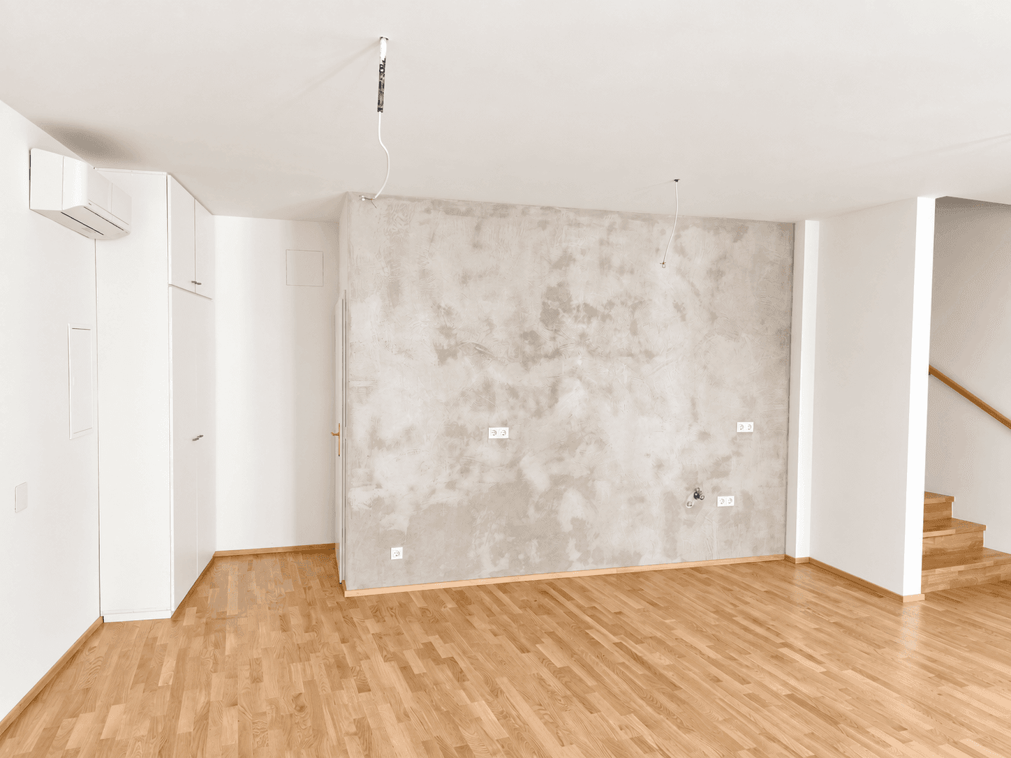 Heller Raum mit Holzboden, einer strukturierten Wand und Einbauschränken.