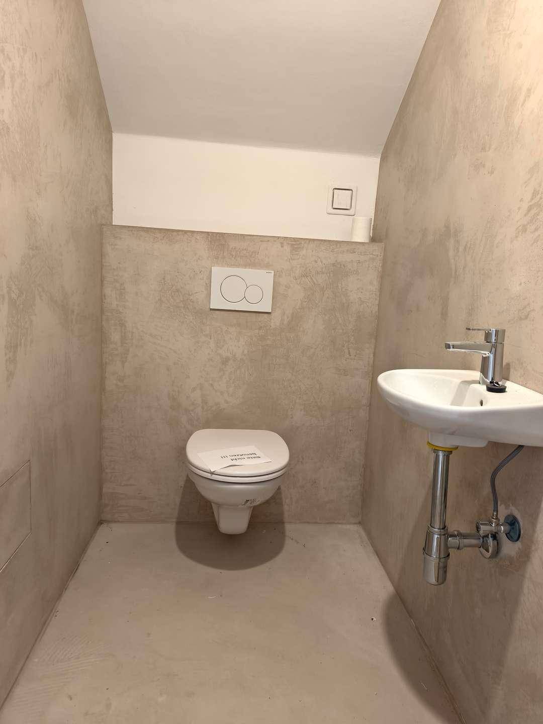 Modernes Gäste-WC mit Wand-WC und kleinem Waschbecken in neutralen Farbtönen.