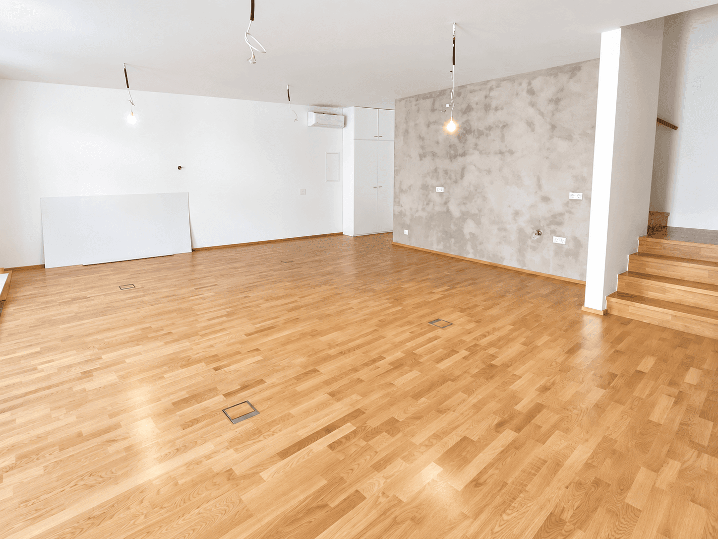 Großer, leerer Raum mit Holzboden, einer Akzentwand und vorbereiteten Anschlüssen.