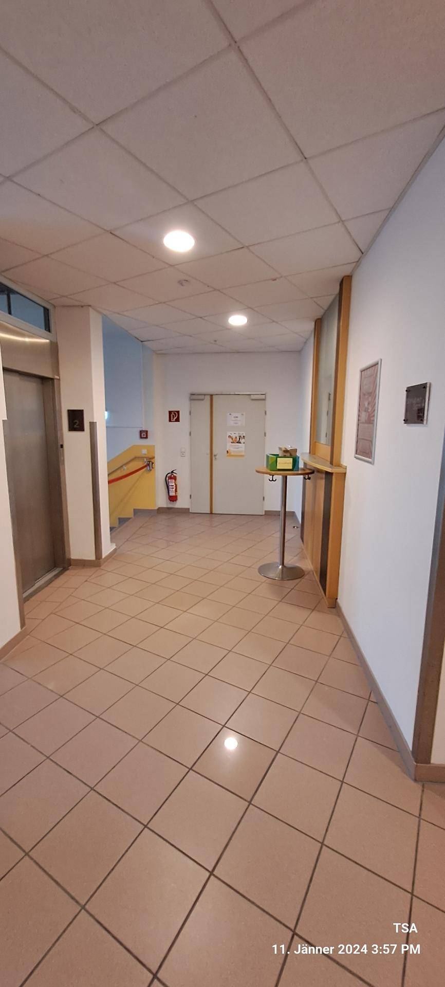 Heller Flur mit Fliesenboden, Aufzug und einer Rampe im Hintergrund, gut gepflegt.