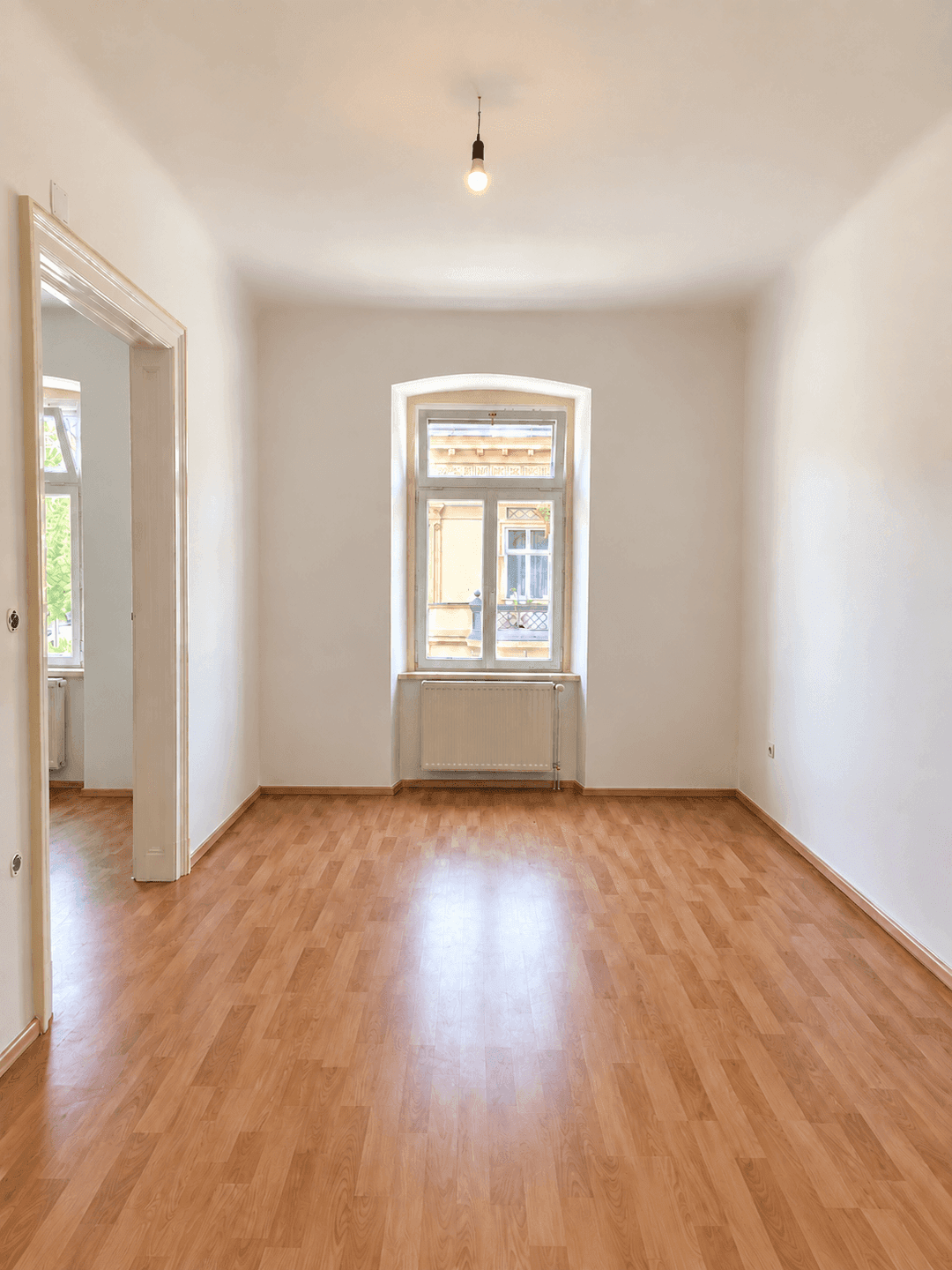 Heller, leerer Raum mit Laminatboden und einem großen Fenster, das den Blick nach draußen ermöglicht.