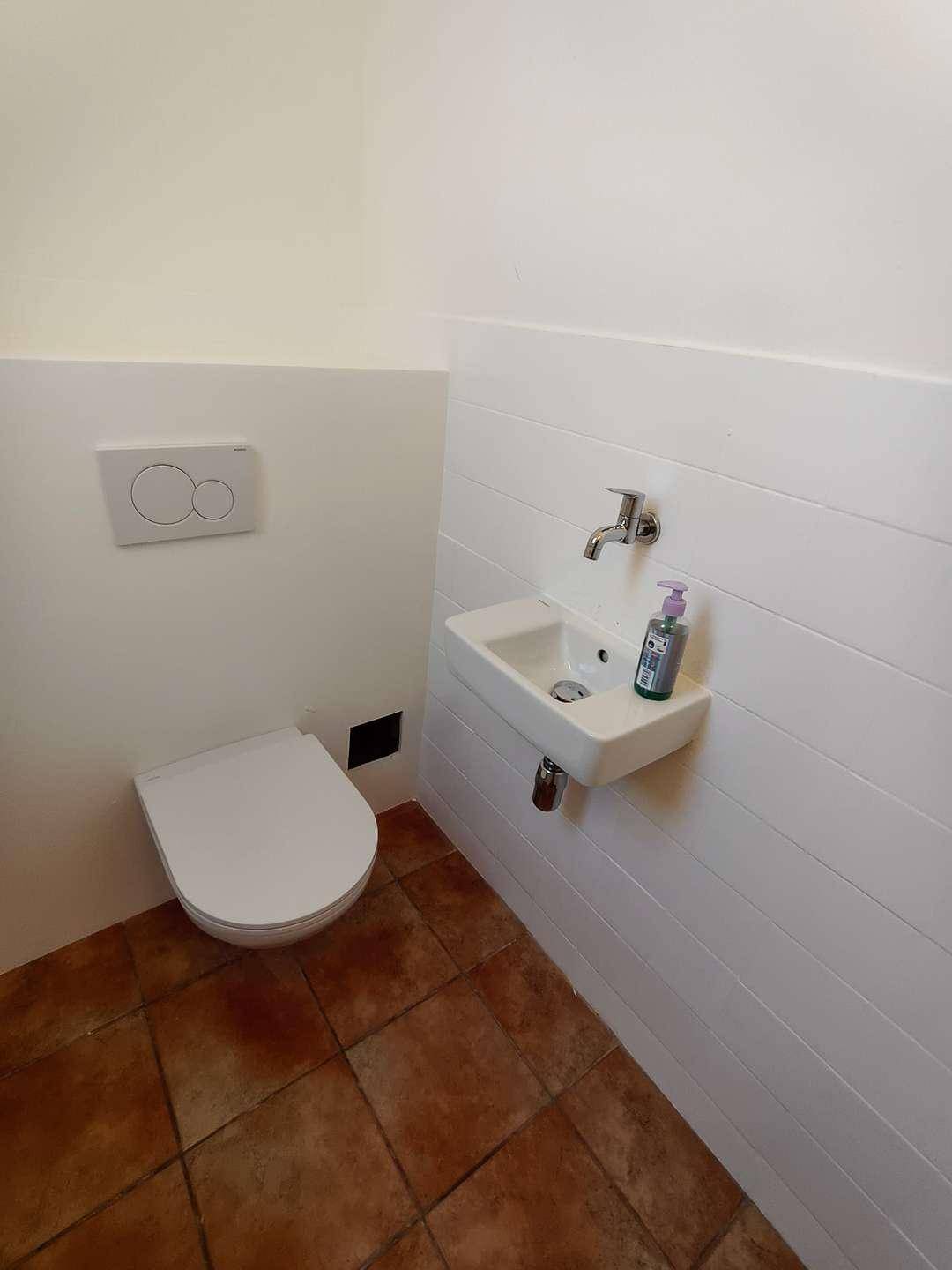 Kleine Gästetoilette mit Wand-WC, kleinem Waschbecken und Terrakotta-Fliesenboden.