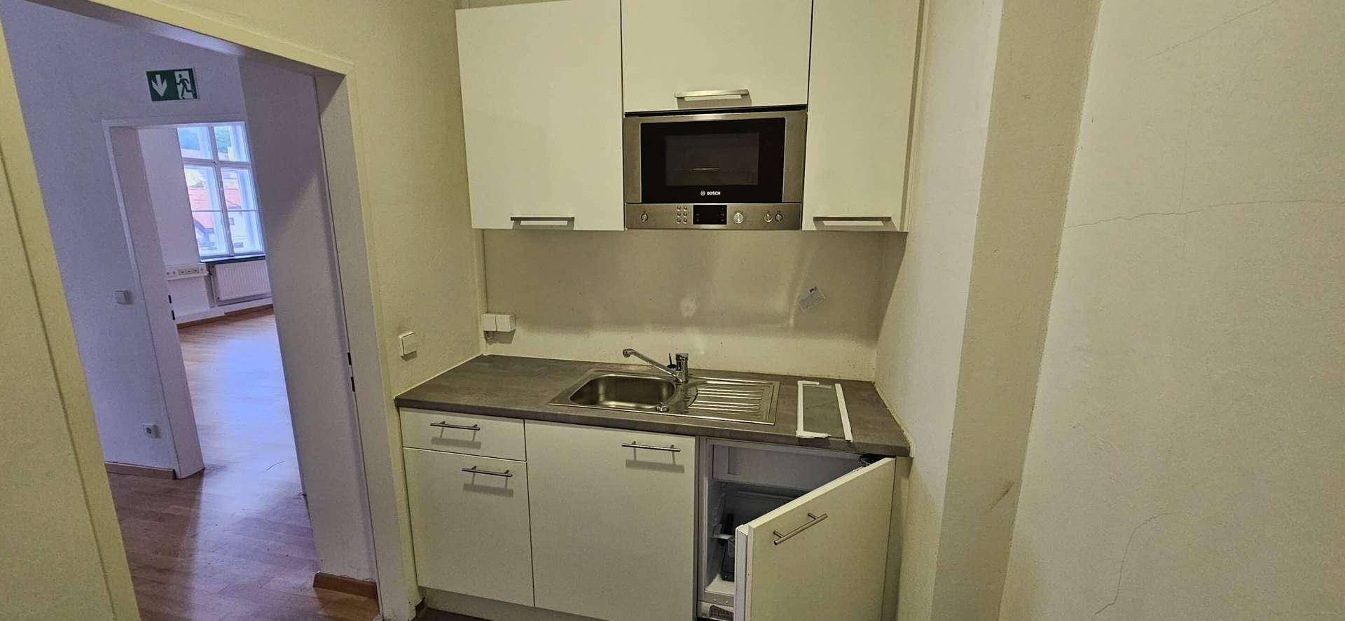 Kleine Einbauküche mit Mikrowelle, Spüle und Kühlschrank in einem Flur.