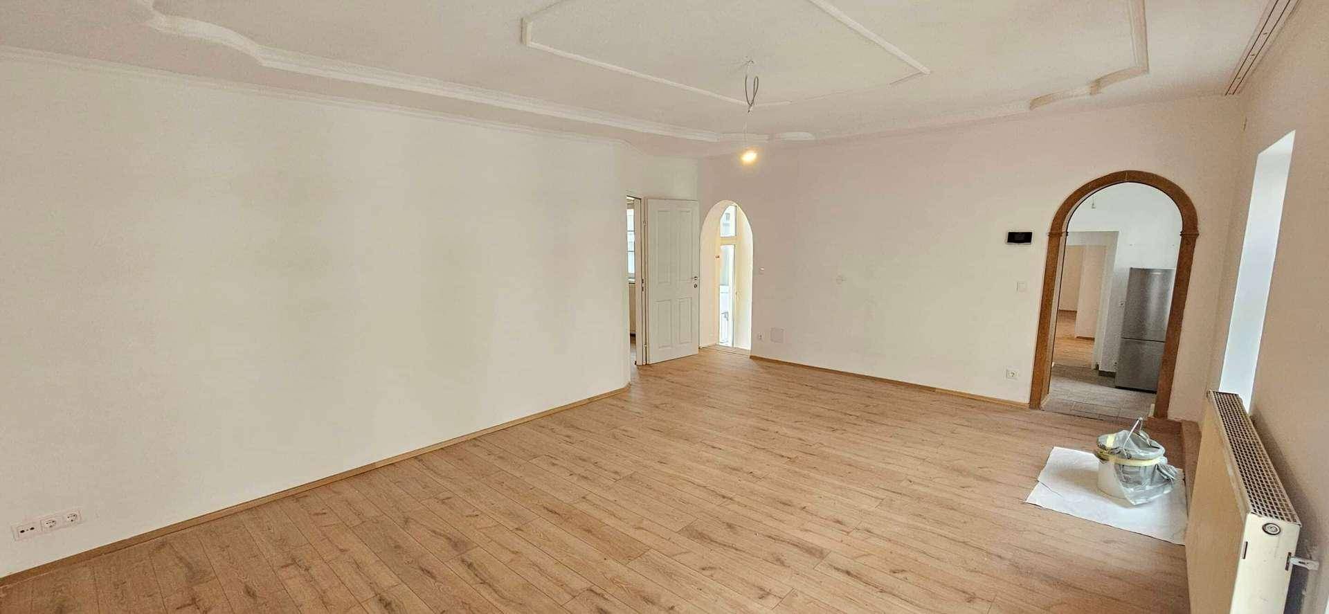 Geräumiges, leeres Zimmer mit Holzboden, weißen Wänden, dekorativer Decke und einem Rundbogen.