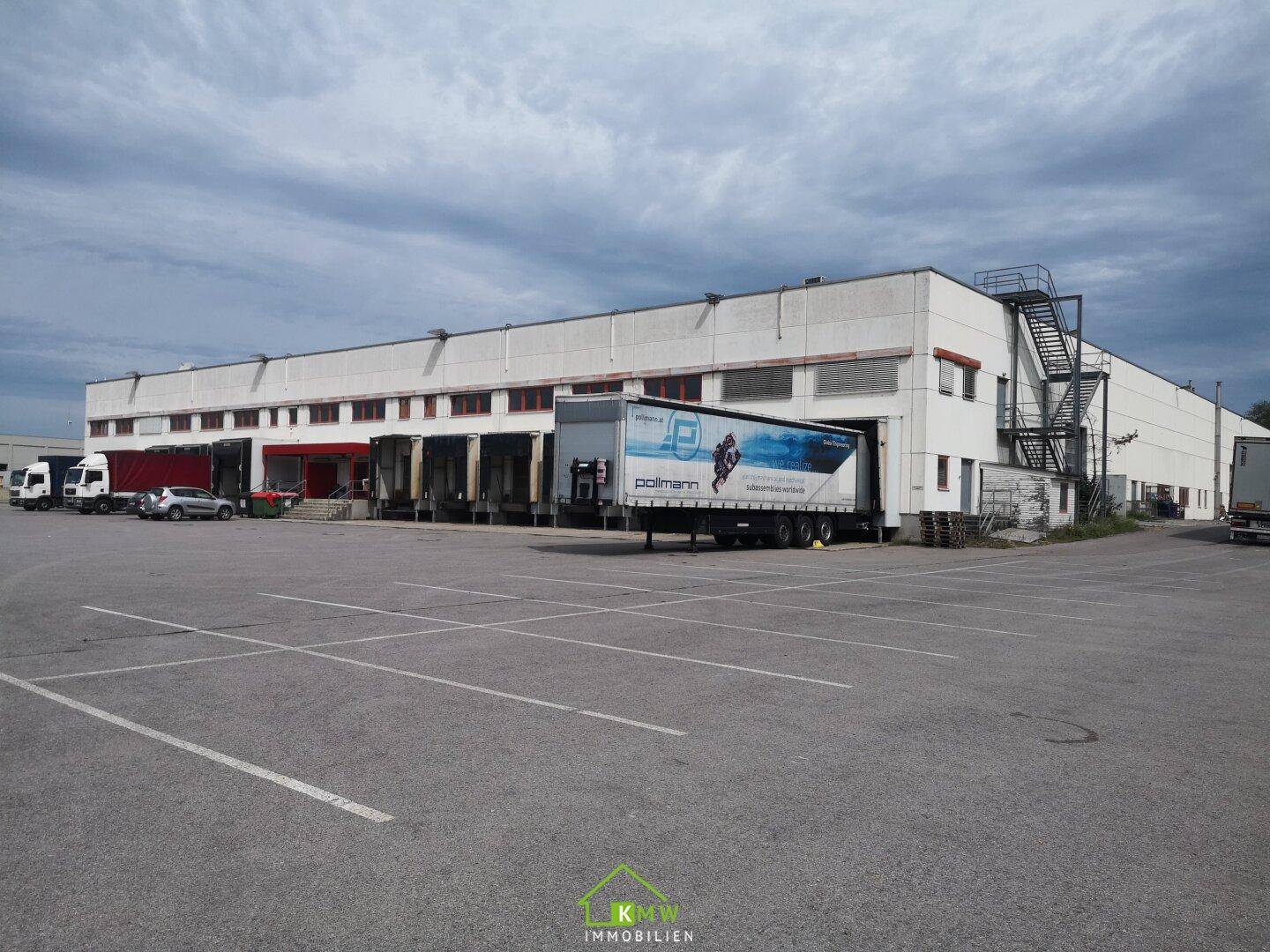 Großes Industriegebäude mit zahlreichen Laderampen und weitläufigem Parkplatz unter bewölktem Himmel.