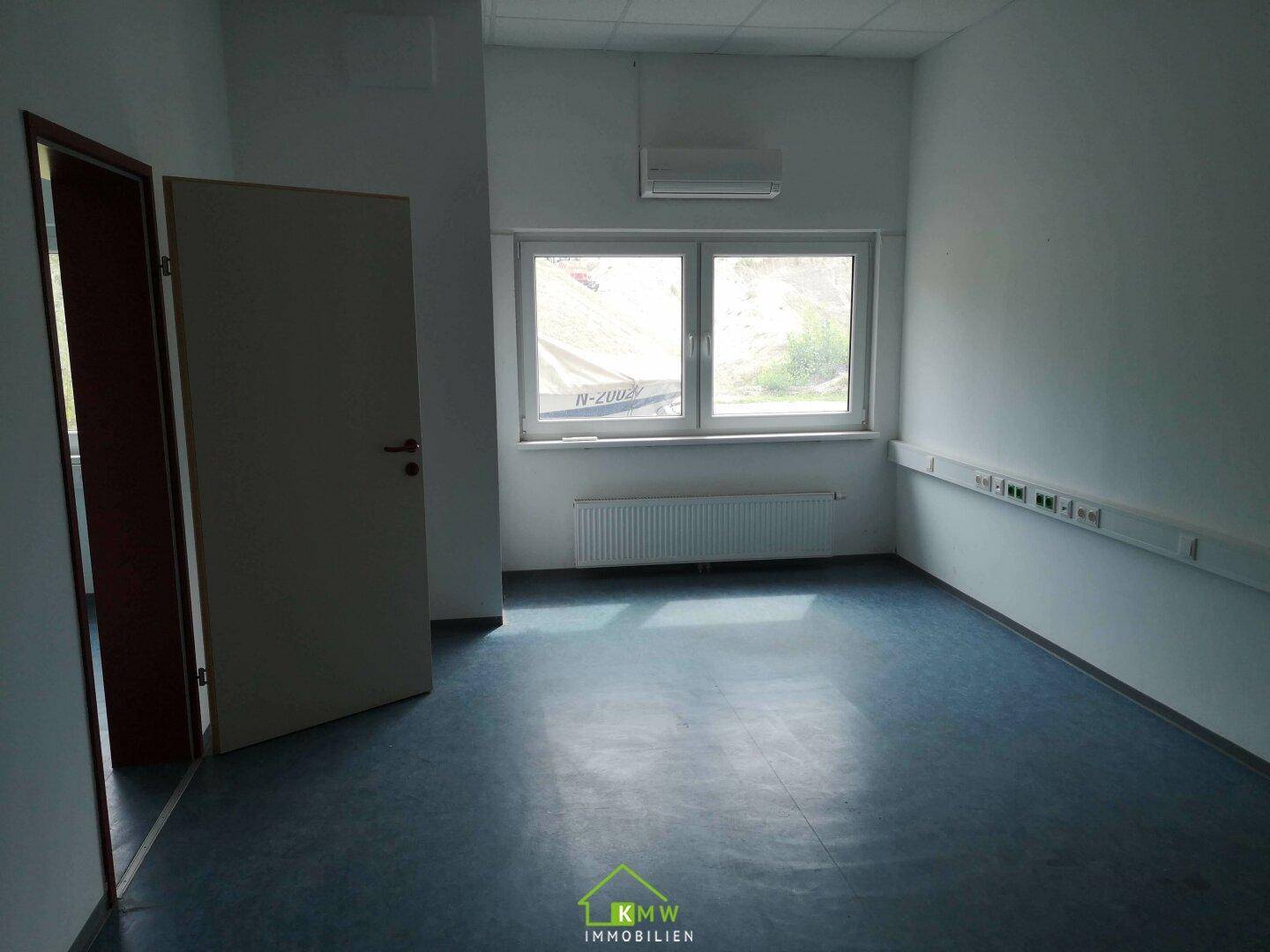 Helles Büro mit blauem Vinylboden, weißen Wänden und Klimaanlage, ausgestattet mit Heizkörper.